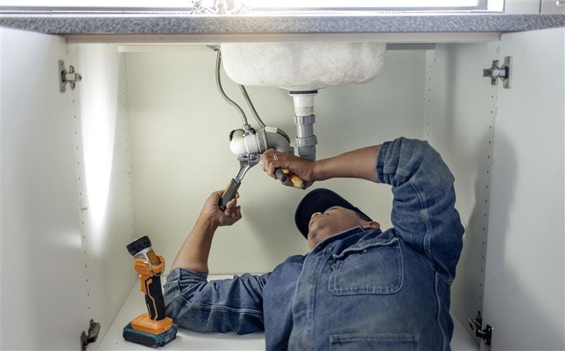 Plumber repairing pipes beneath a bathroom sink in Temple City